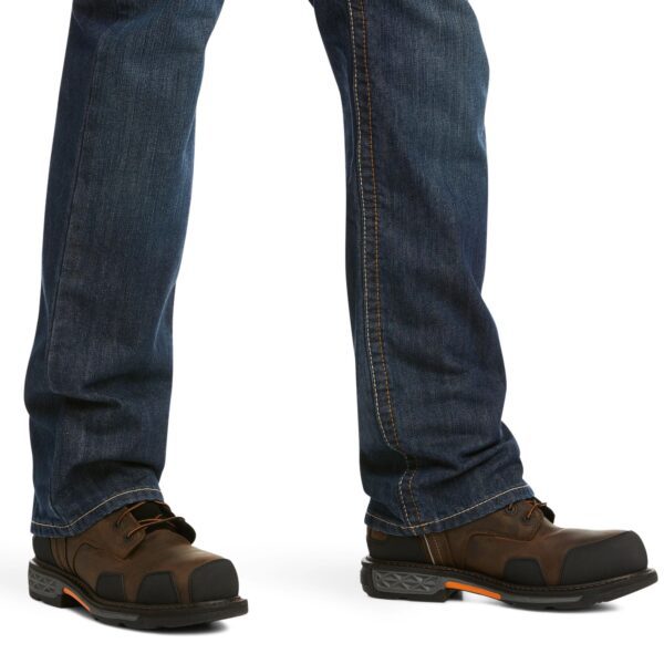 A person standing in jeans and boots with one foot on the ground.