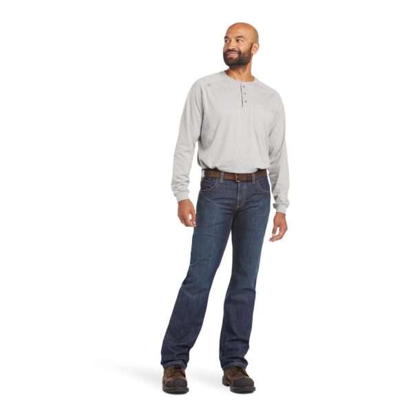 A man standing in jeans and boots with a beard.