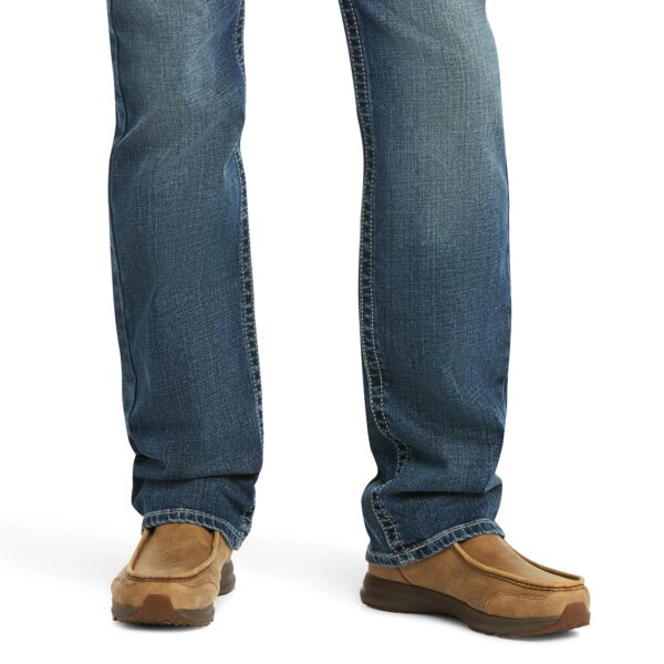 A person standing in jeans and shoes with one foot on the ground.