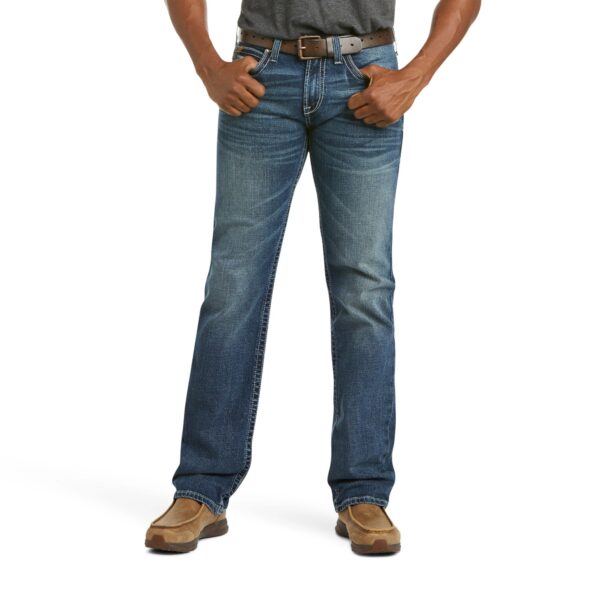 A man wearing jeans and boots is standing with his hands in his pockets.
