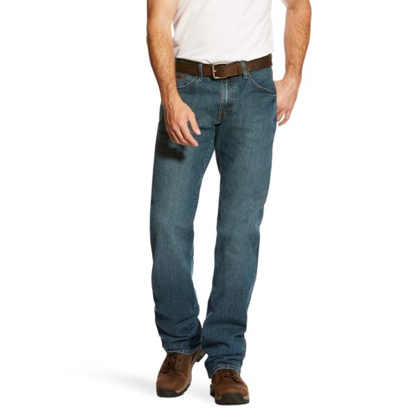 A man wearing jeans and boots is holding his hand in his pocket.