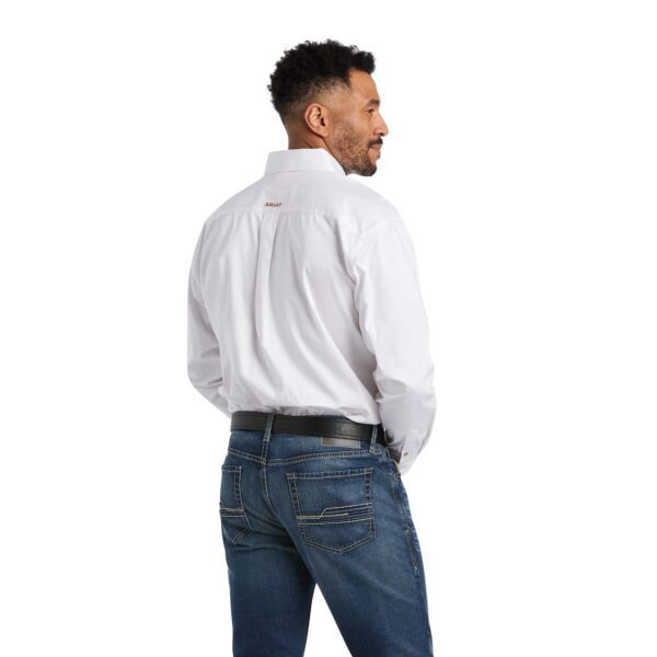 A man in white shirt and jeans standing next to wall.