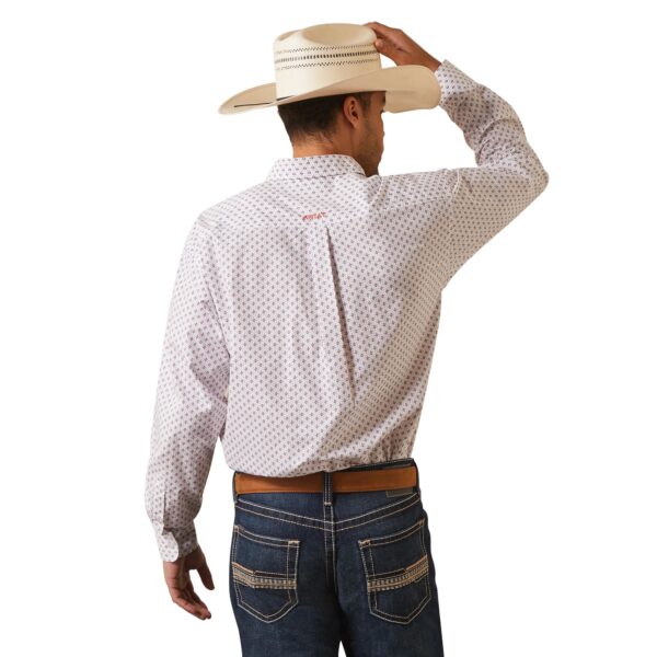 A man in white shirt and hat holding his hand up to the side of head.