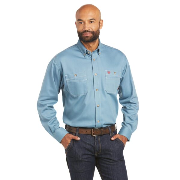 A man in blue shirt and jeans holding his hands in his pockets.