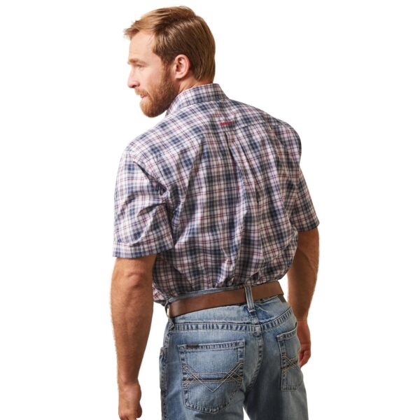 A man in jeans and plaid shirt standing next to wall.