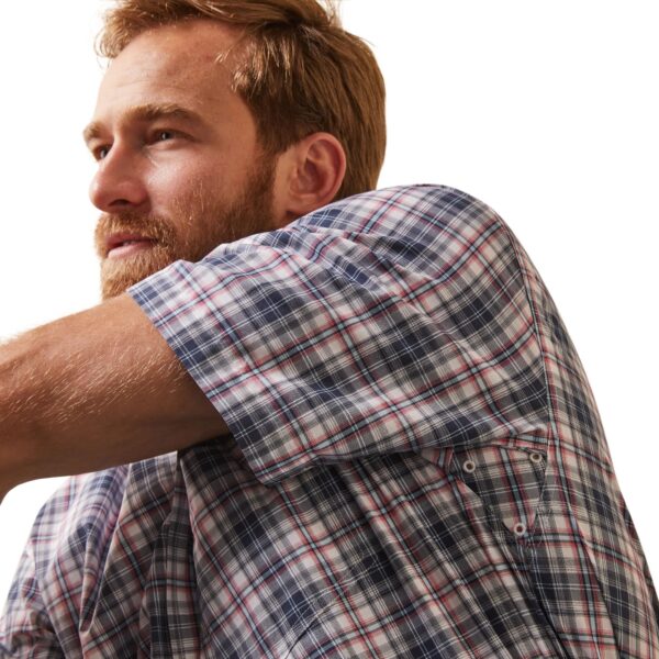 A man in plaid shirt leaning on wall.