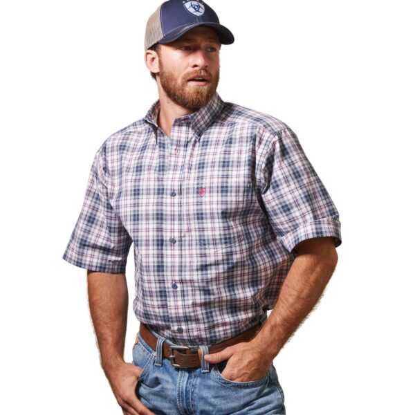 A man in plaid shirt and hat standing with hands in his pockets.