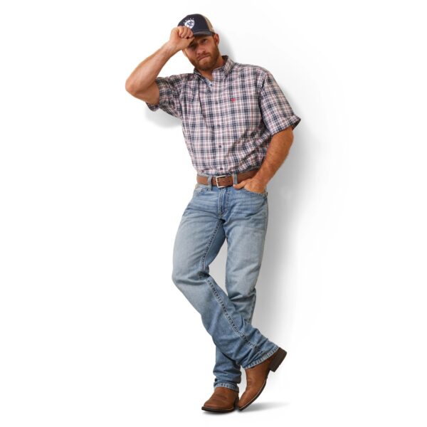 A man in plaid shirt and jeans standing next to wall.