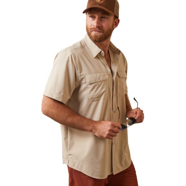 A man in brown pants and a tan shirt holding a cell phone.