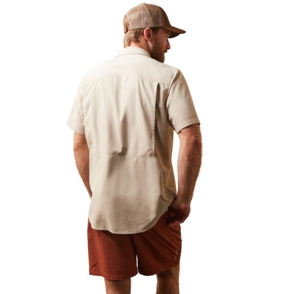 A man in shorts and hat standing next to a wall.