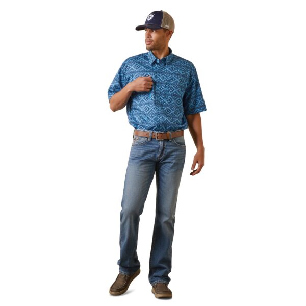 A man in blue shirt and hat standing next to wall.