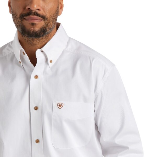 A man wearing a white shirt with a brown button down collar.